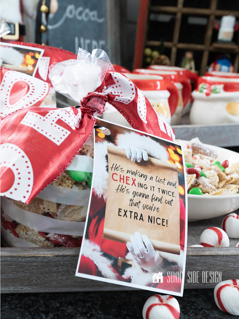 Festive Gift Idea for Neighbors, Peppermint Christmas Chex Mix in clear cellophane bags tied with a red and white "HO HO" ribbon and a free printable gift tag. More Peppermint Christmas Chex Mix in a bowl on a grey tray with additional peppermint candies.