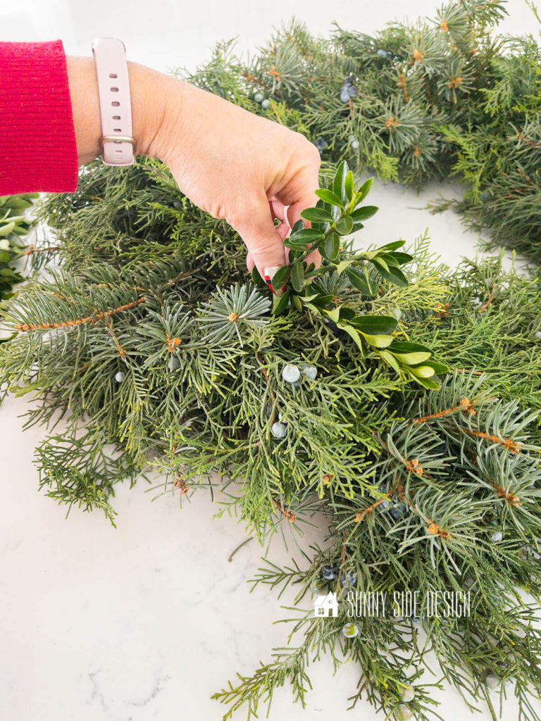 Fresh evergreens are secured to a wire wreath form with green paddle wire.