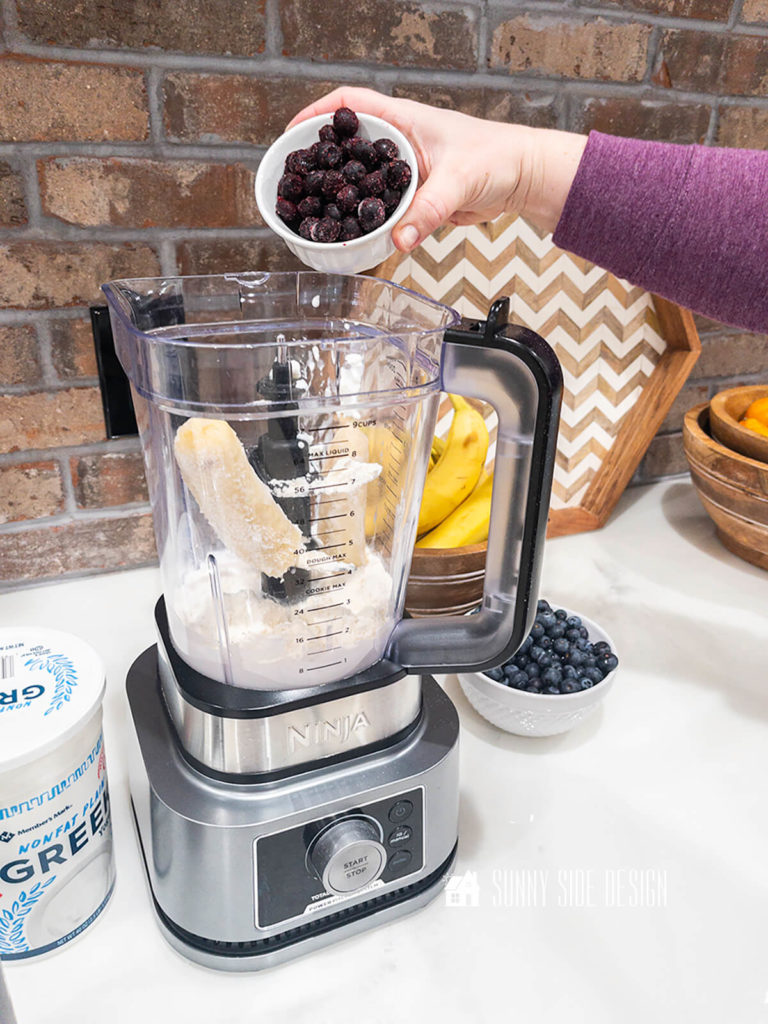 Woman's hand pouring a bowl of frozen blueberries into the blender for the healthy smoothie