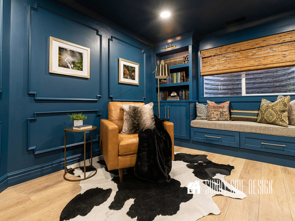 Home improvement ideas, elegant paneled walls in a deep blue with built in bookshelves, window seat, leather reading chair, cozy cow hide rug.