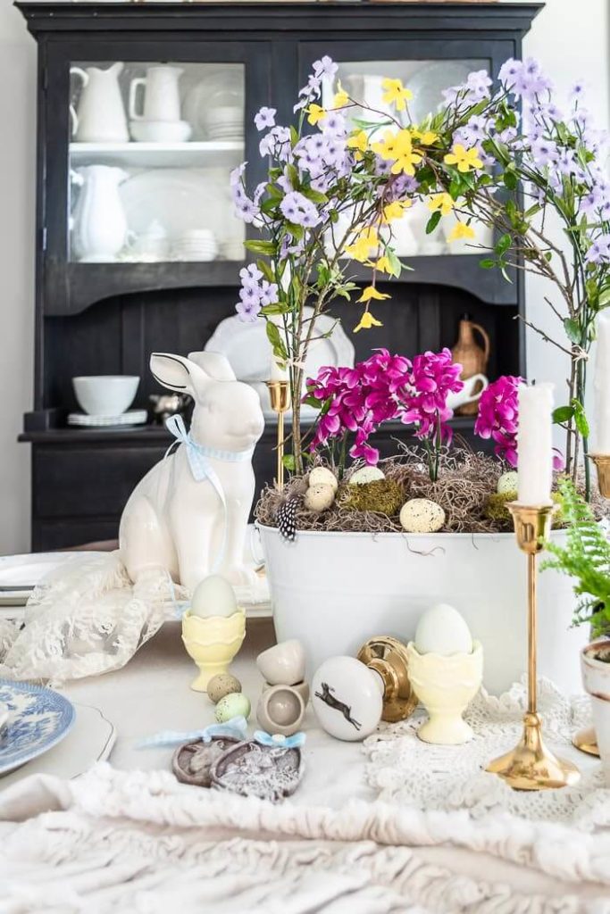 Easter basket centerpiece with flowers and eggs look pretty on this spring inspired table.