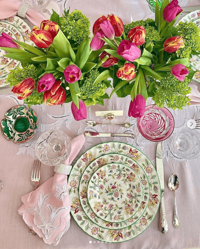Cottage inspired spring table with fresh tulips and floral dinnerware on a pink tablecloth.