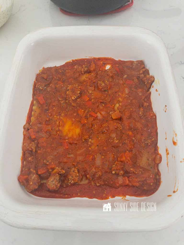 First layer of meat sauce is placed over the dry lasagna noodles.
