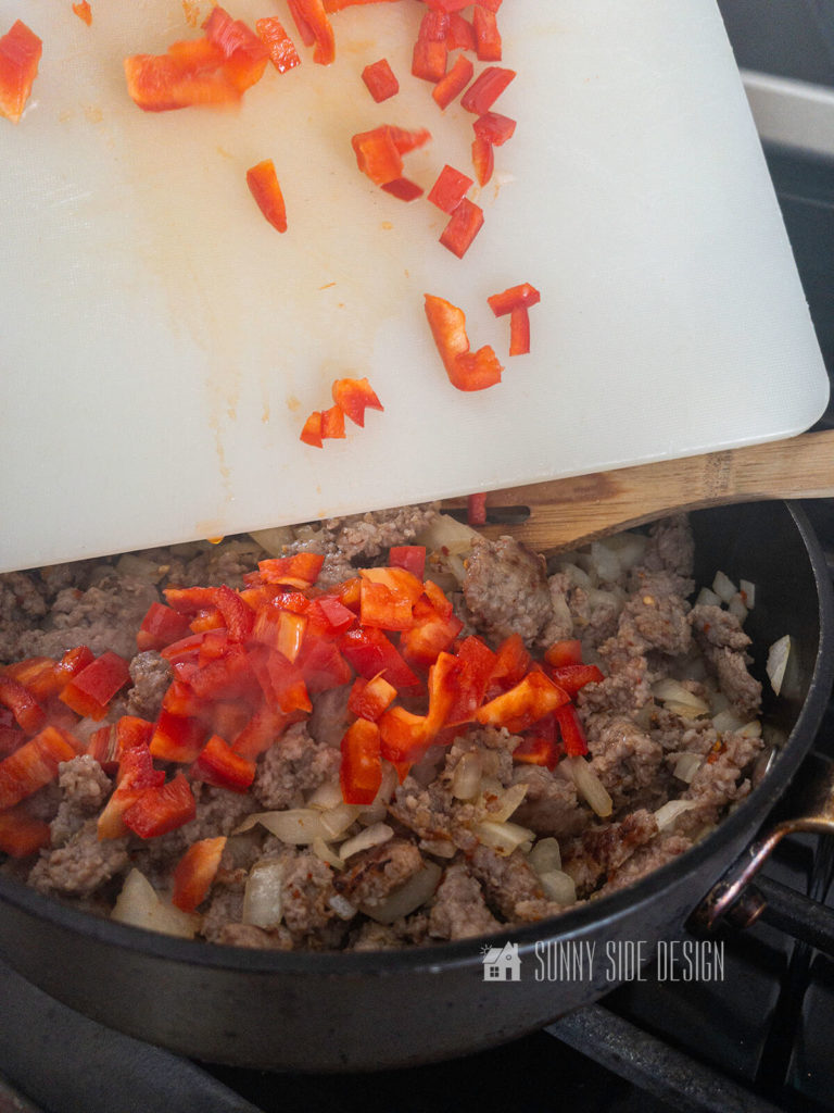 Add diced red bell pepper to browned sausage and onions.