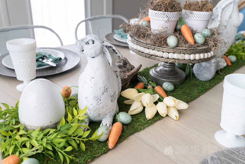 Easter tablescape with moss table runner, carrots, tulips eggs and bunnies.