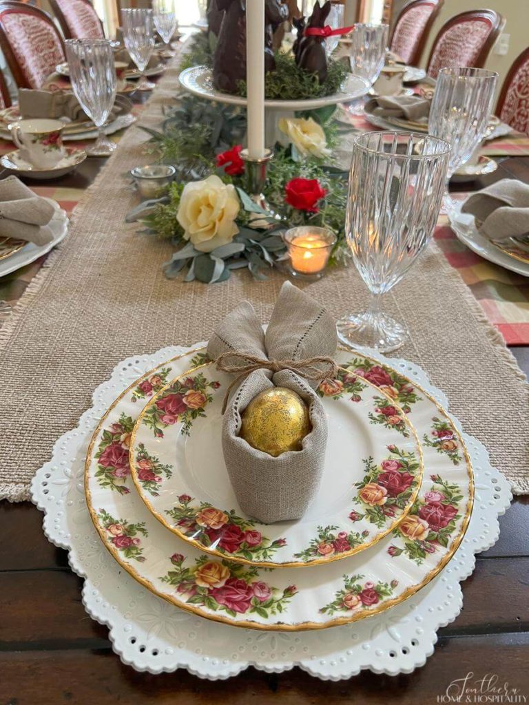 Cottage inspired Easter tablescape with floral places on white chargers, linen table runner with a faux chocolate bunny centerpiece.