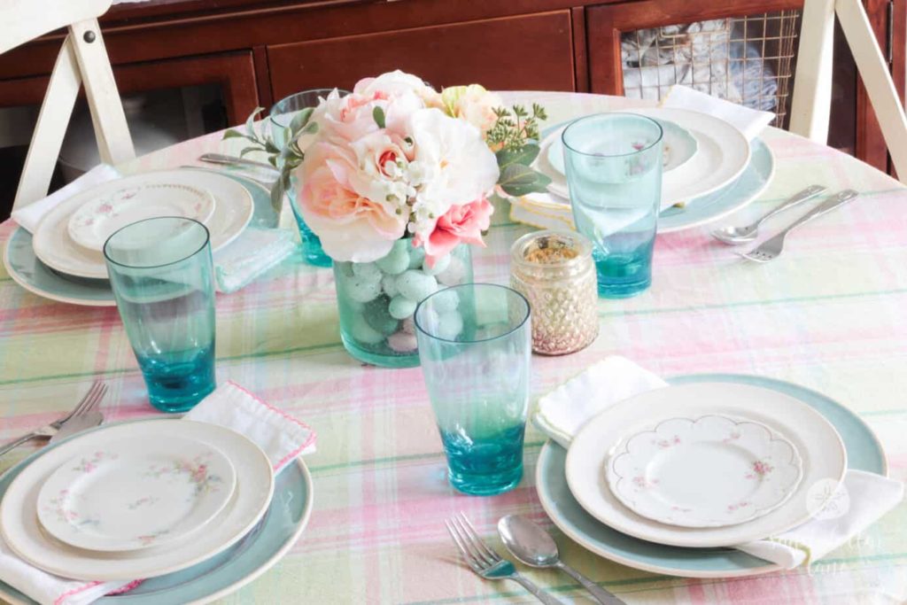 Spring table decor ideas: pastel plaid tablecloth paired with pastel blue and floral dinnerware, blue glassware and a pretty floral centerpiece.