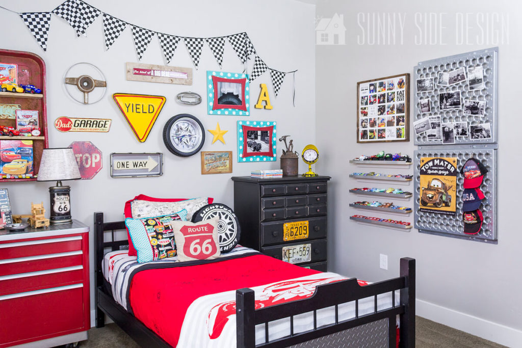 Little boys car themes bedroom with gallery wall above black painted bed with vintage car parts, photos, checkered flag, car themed bedding.