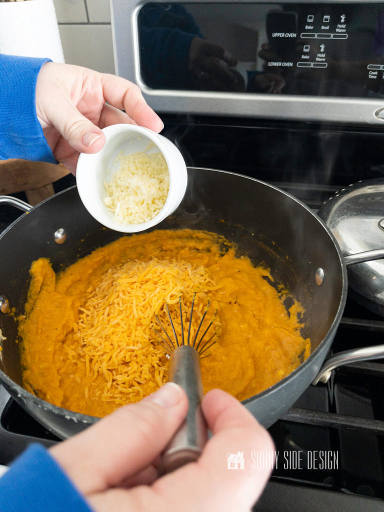 Add cheddar cheese and Parmesan cheese to the pureed butternut squash in a heavy pan on the stovetop.