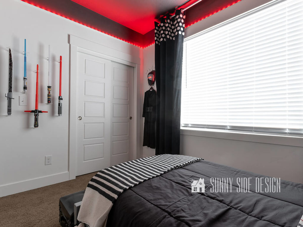 Red LED lights concealed with cove moulding and a black dyed curtain with white polka dots, light sabers mounted o the wall, Kylo Ren costume hung on wall with black and white bedding.