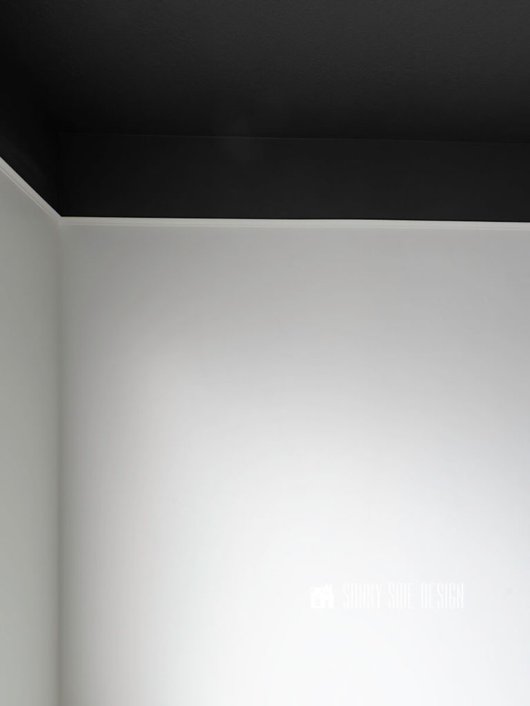 White painted cove moulding separate black and white paint on wall. The cove moulding is used to hide the LED strip lights on the wall.