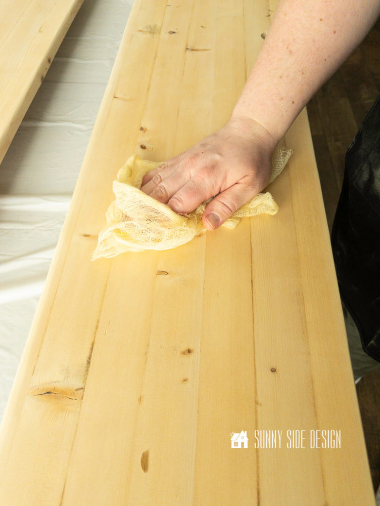 How to stain pine wood, woman's hand holding a tack removes dust from pine board before applying pre-stain wood conditioner.