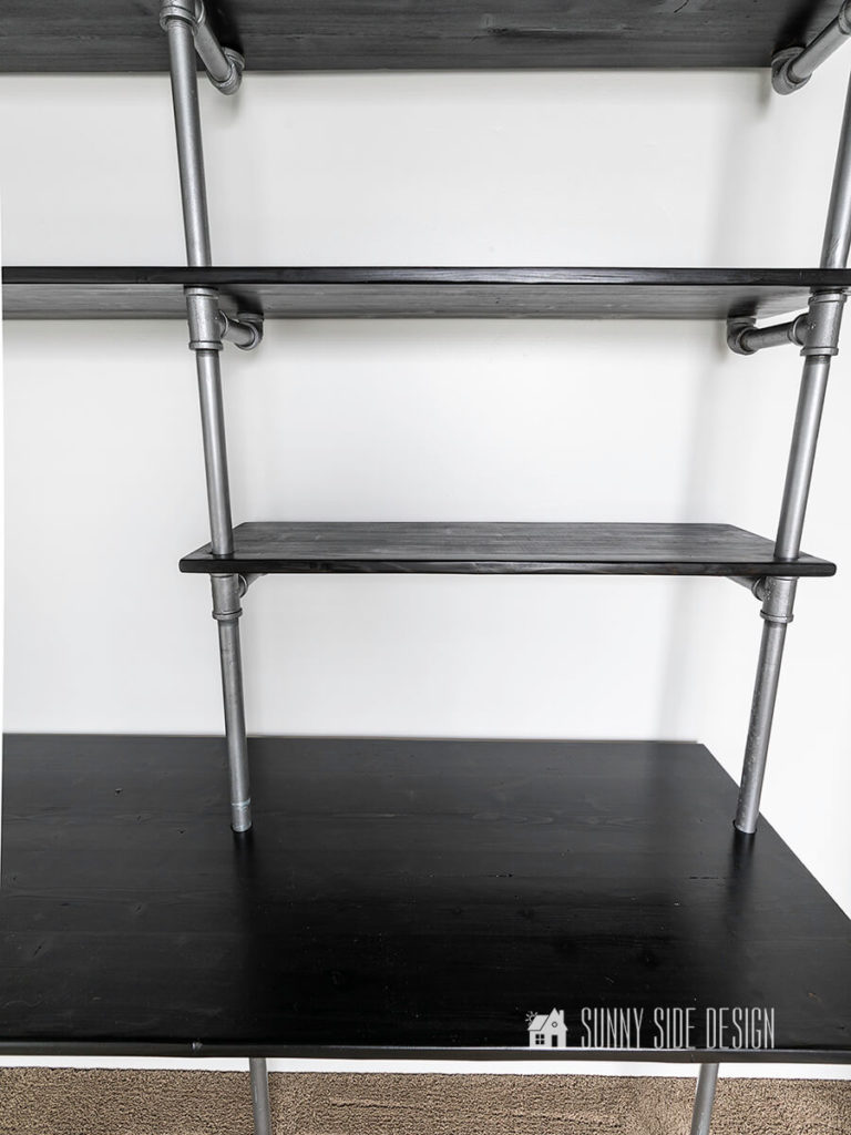Close up view of desk top with shelves and metal pipe for supports.