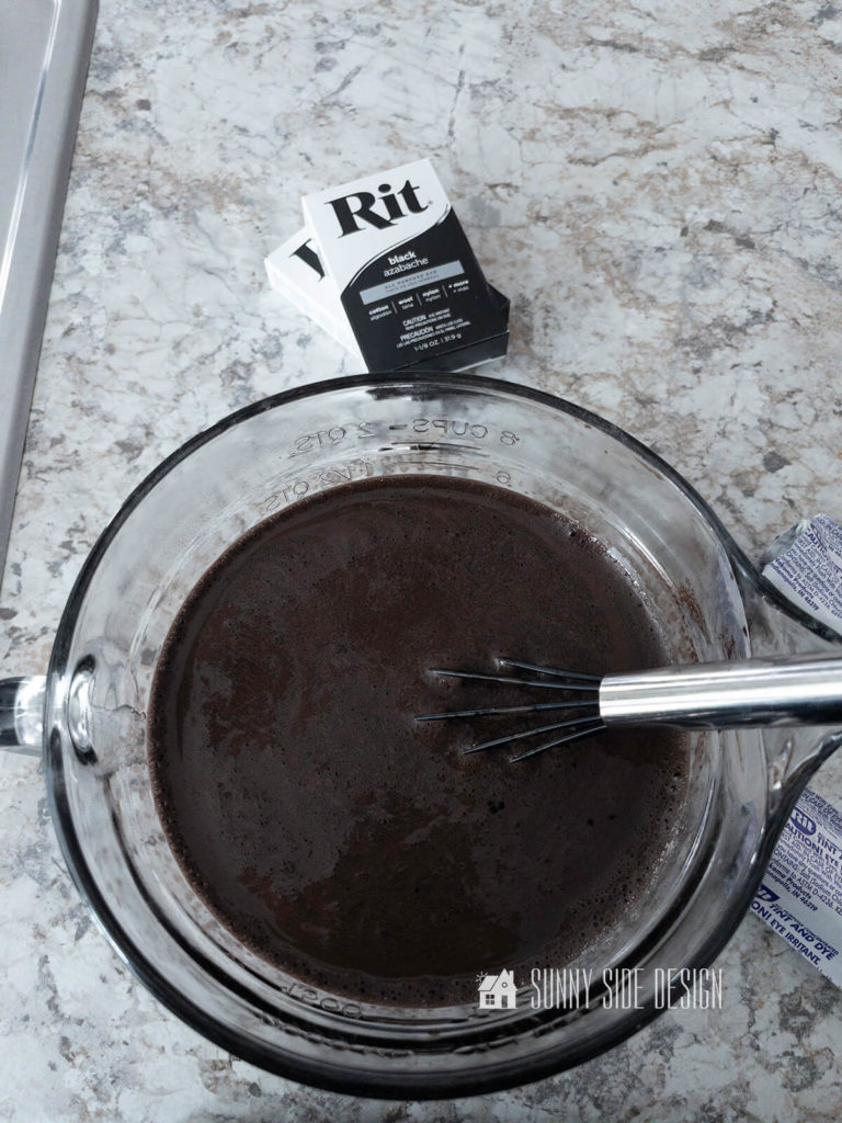 Black powdered Rit Dye is dissolved into how water in a large measuring cup with a stainless steel whisk.