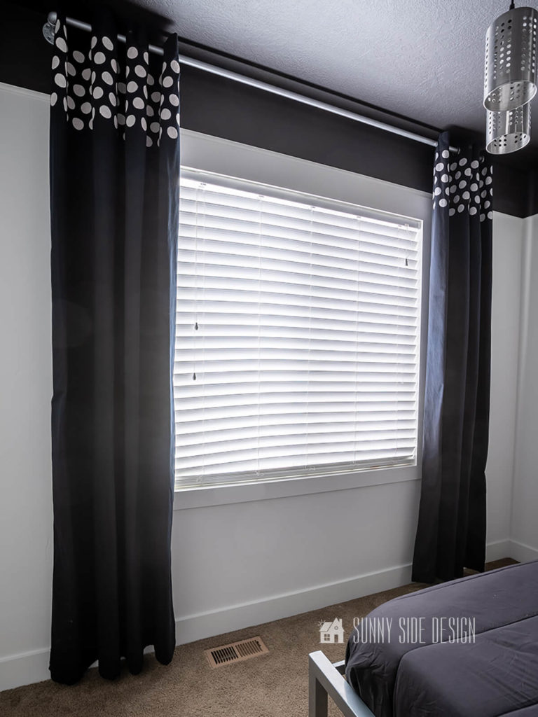 Black dyed drapery panels hung on a white wall with a black boarder at ceiling.