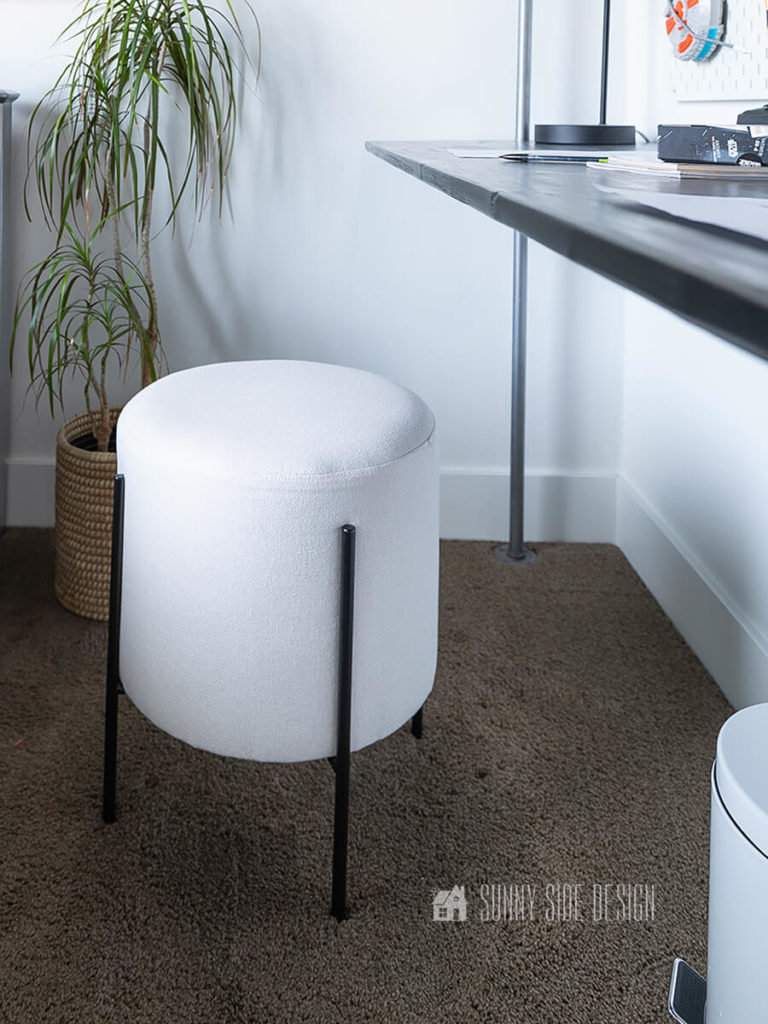 White stool with black metal legs is placed at wood and pipe desk with shelves.