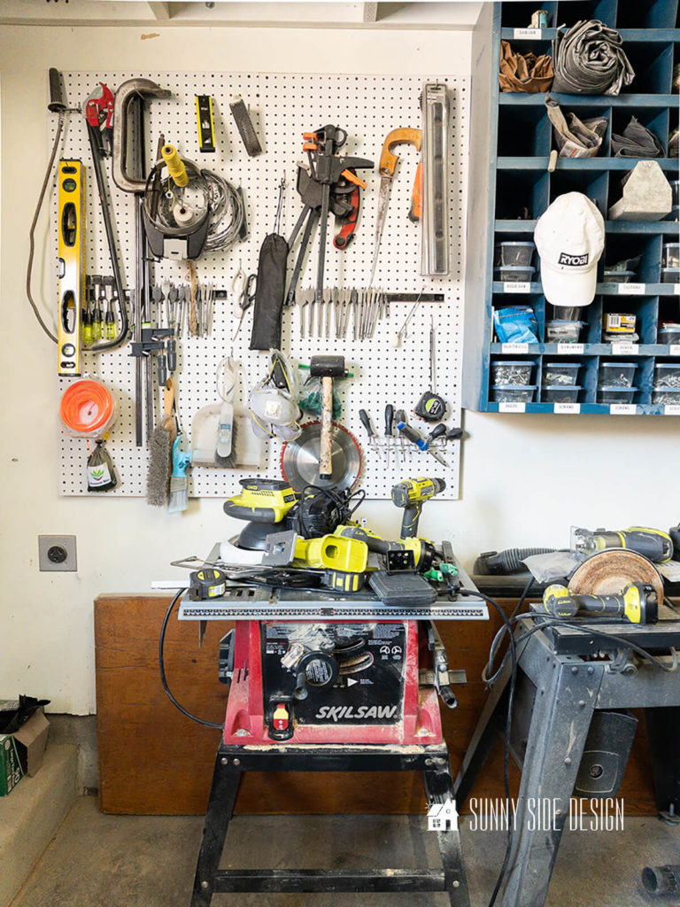 Garage wall before makeover with Ryobi links products with a pegboard wall holding a variety of tools. Power tools are set on the table saw and bench sander.
