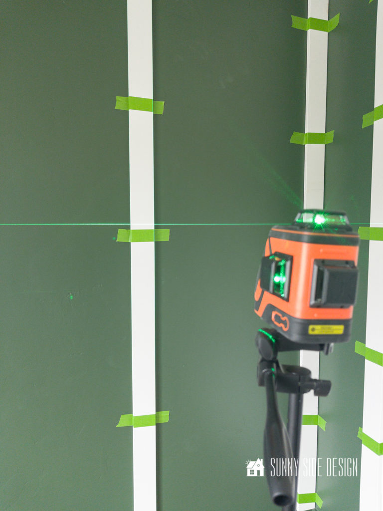 Laser level projecting onto a painted green wall for placement of horizontal boards for a DIY board and batten wall.