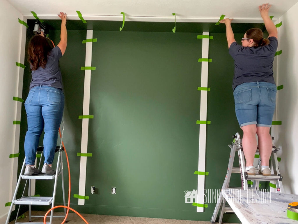 Two women placing board at ceiling and securing with a brad nailer.