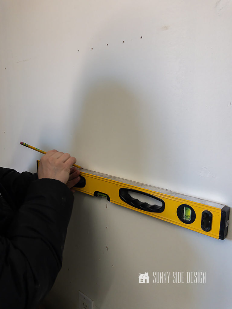 Woman holding a level marks wall before installing garage wall storage product.