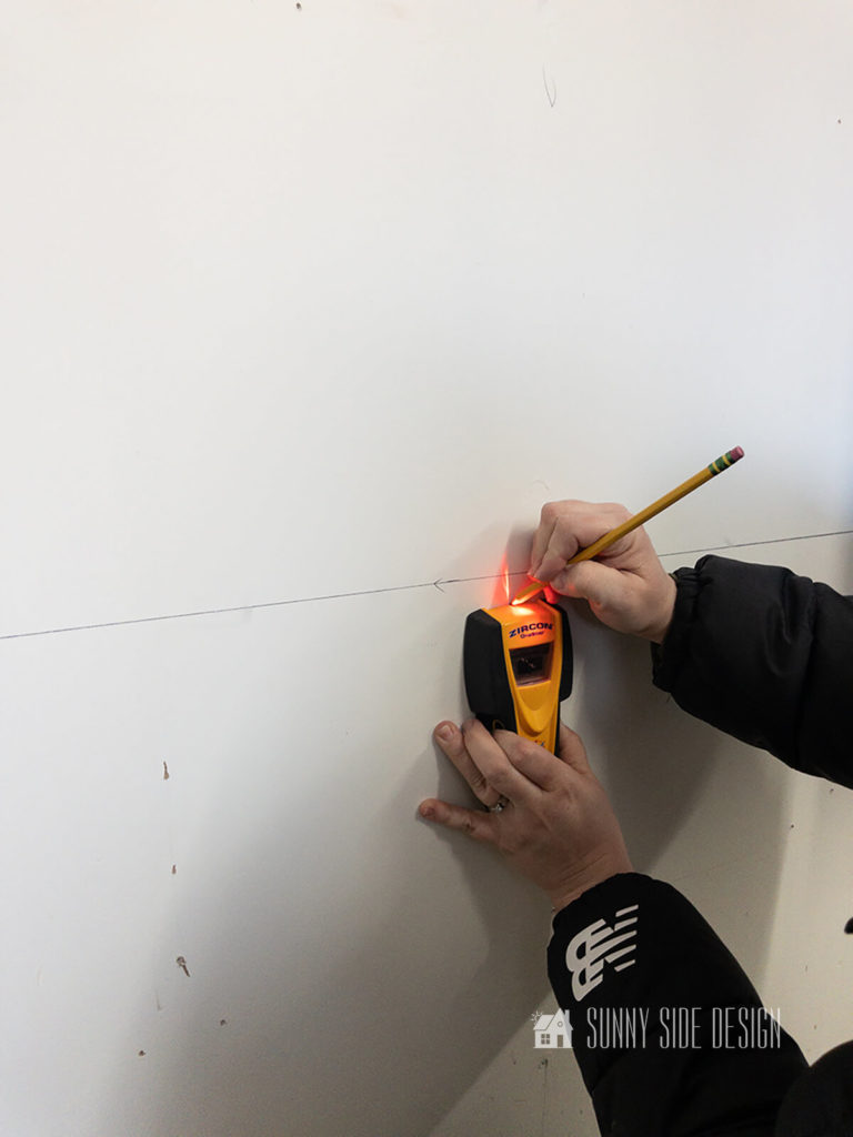 Woman holding a stud finder and pencil, marks the studs in the wall.