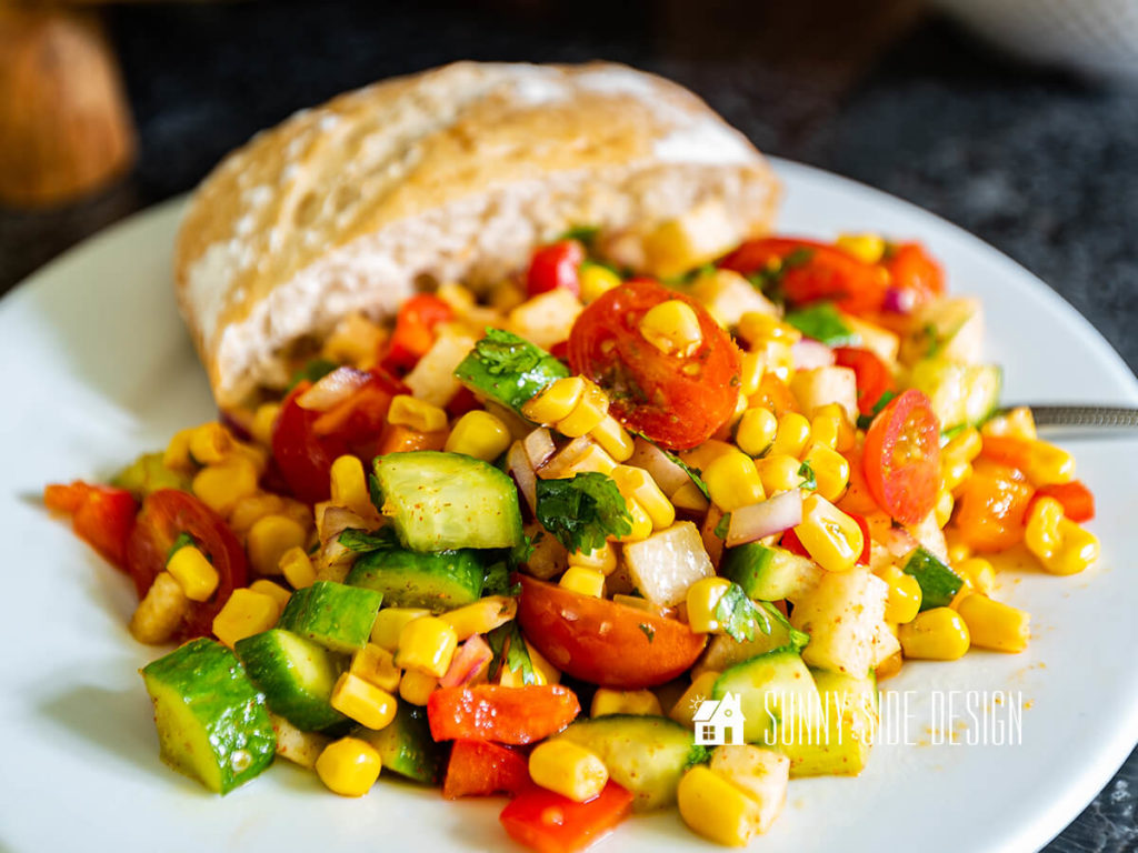 Easy corn salad recipe on a white plate with a roll.