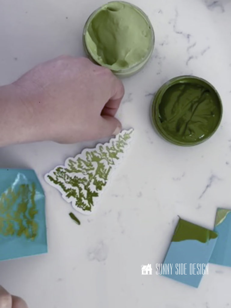 Woman hand removing chalk transfer from tree shape with two shades of green chalkology paste.