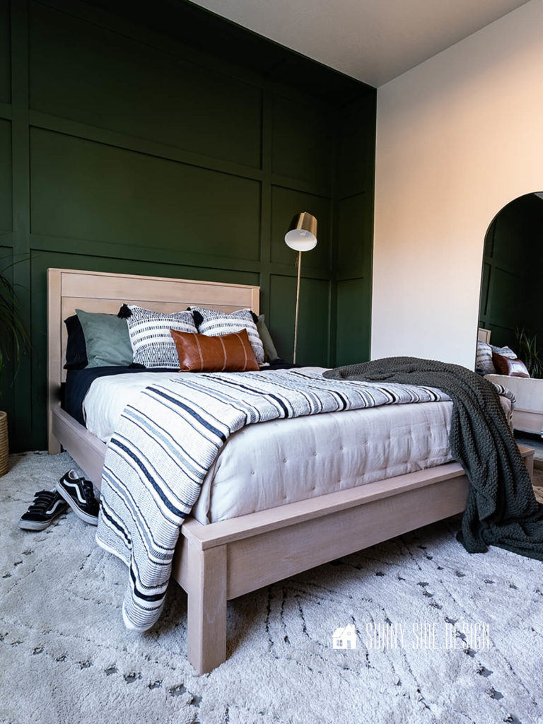 Faux rifted oak bed frame with a green board and batten wall and black and white bedding with green and leather accents.