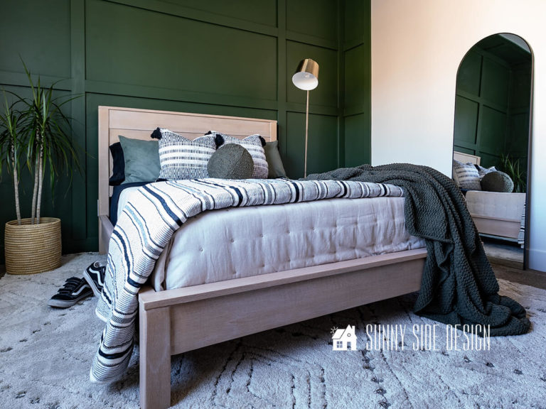 Faux rifted oak bed frame with a green board and batten wall and black and white bedding with green and leather accents.