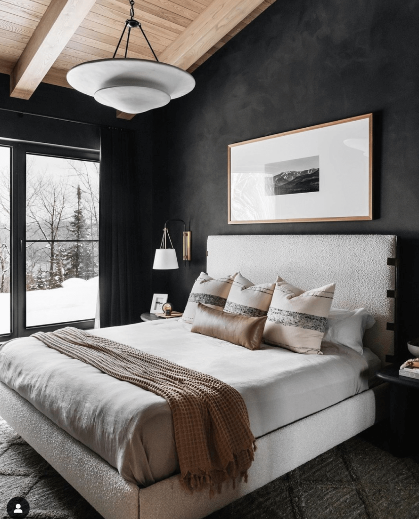Men's bedroom ideas, a neutral palette of black, brown, gray, creamy white and natural wood give this bedroom a cozy and relaxes masculine vibe. Walls are black venetian plaster, with a natural plank wood and beam ceiling, upholstered creaming white bed with leather accents layered with neutral bedding and pillows.