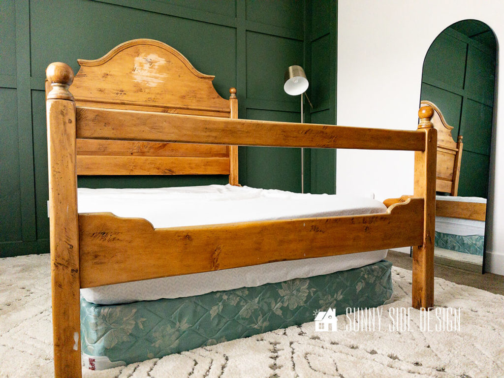 Wooden bed frame before modern makeover in a bedroom with a forest green board and batten wall.