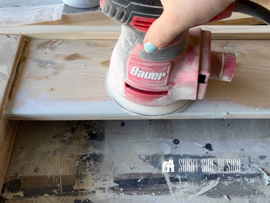 An orbital sander sands bondo areas on the makeover footboard for the bed frame.
