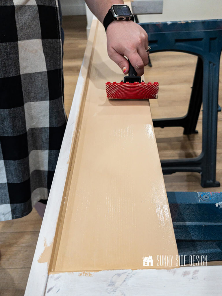 A wood grain tool is pushed through the wet paint to add a faux wood grain texture to the bed frame.