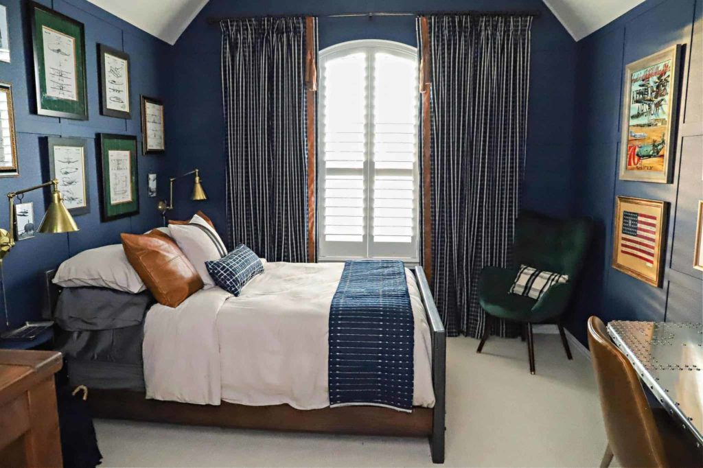 Create a masculine interior with a blue and grey color scheme. Use geometric textile patterns such as stripes and plaids. A dark navy blue is used for the wall color creating a cozy relaxed vibe. Curtain panels are embellished with faux leather accents and tassels.