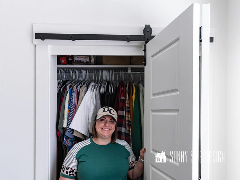 Woman standing with sliding bifold barn door hardware installed on bedroom closet doors.