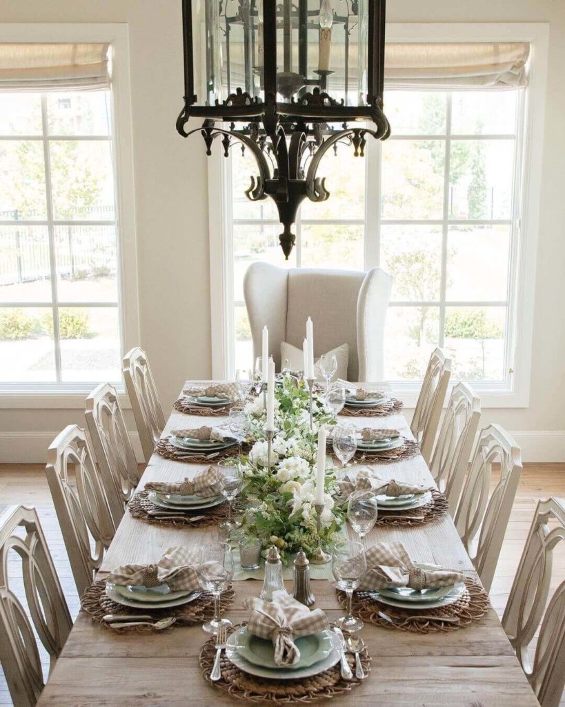 Farmhouse style Fall Tablescape with natural woven placemat o a rustic wood table topped with white and light blue plates, tan gingham napkin with a white floral centerpiece with white taper candles.