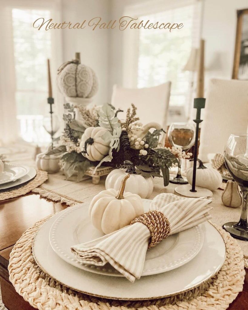 Neutral Fall Talescape with black candlesticks with taupe candles, a variety of neutral pumpkins on a linen table runner. Each place setting is on a natural woven placemat with white plates, taupe and cream striped napkin with a woven napkin ring and a white pumpkin.