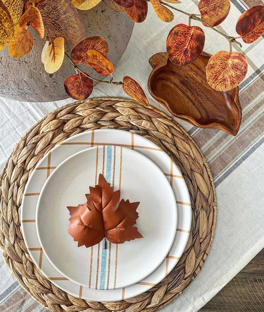 Farmhouse Fall Tablescape with a brown, white, grey plaid table cloth, fall colored eucalyptus and each place setting is on a hyacinth placemat with blue, brown, white plaid dishes.