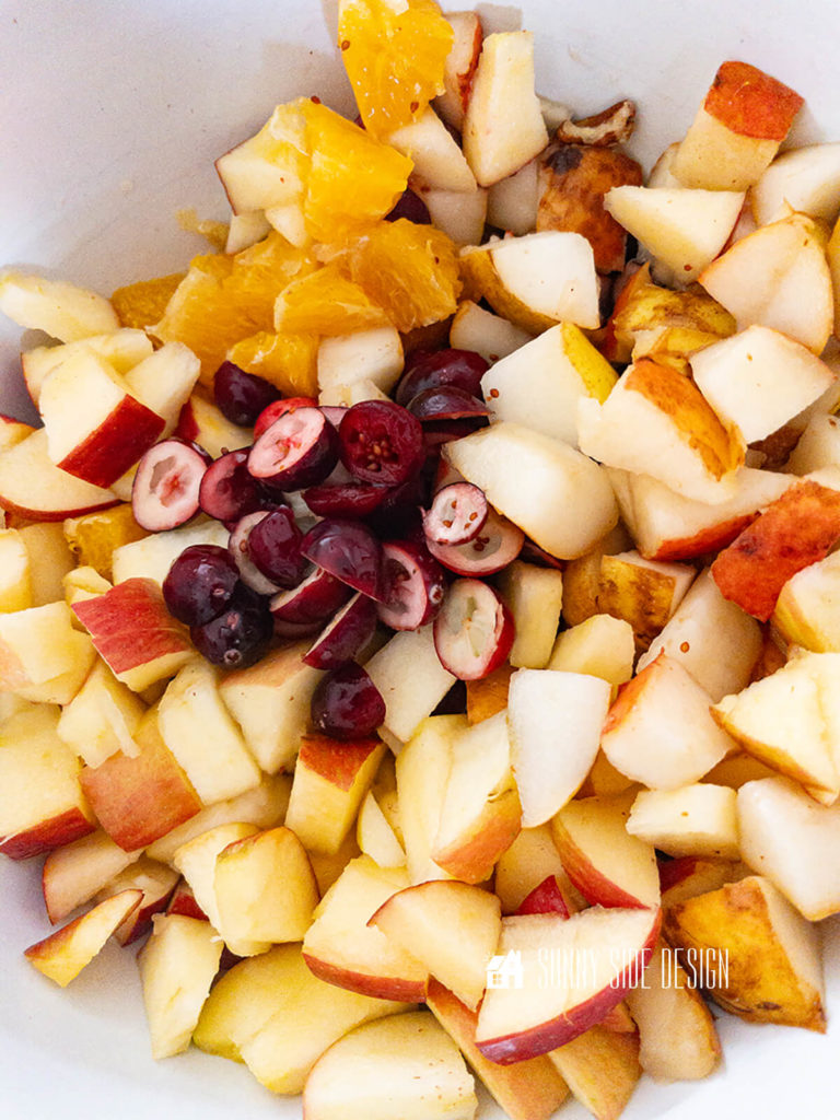 Diced apples pears, oranges and halved cranberries in a bowl.