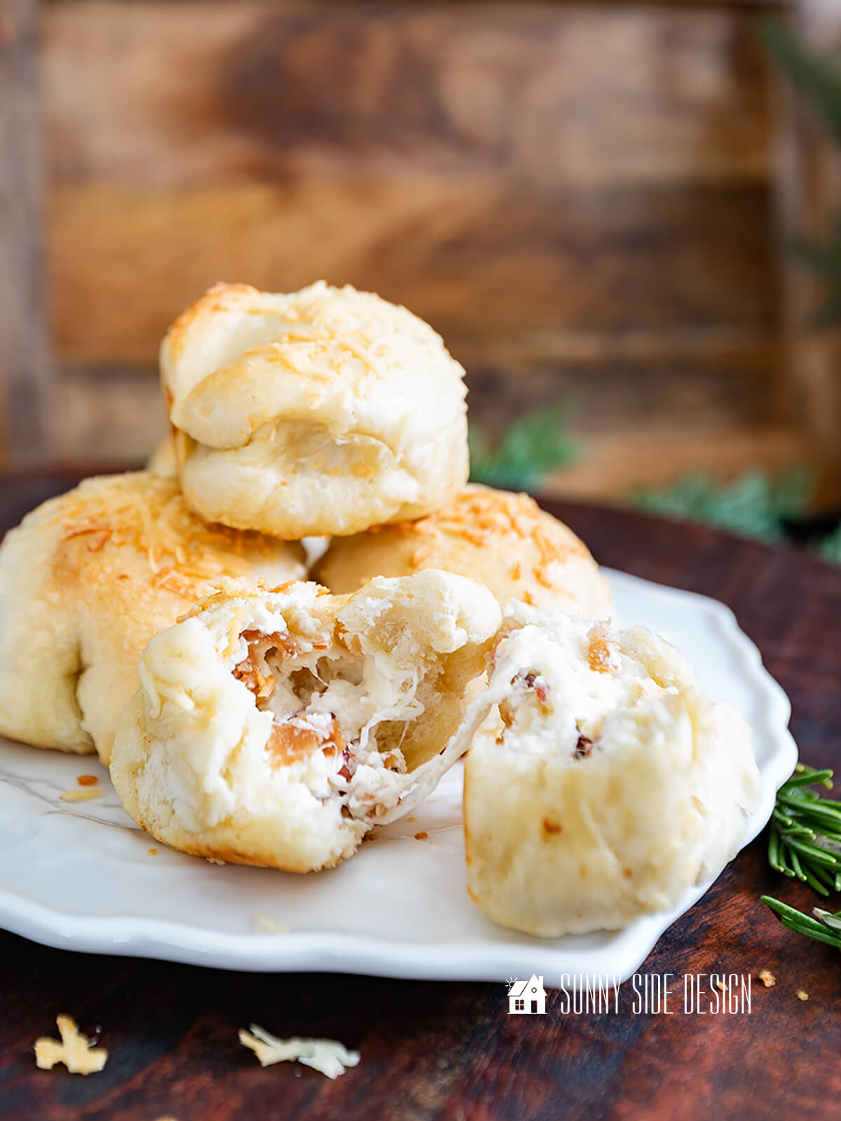 Stacked cheesy bacon bombs on a white plate, one is split open with cheese and bacon spilling out.