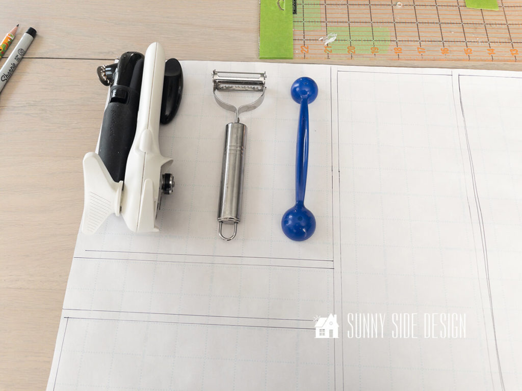Paper is used to create a plan for kitchen drawer organization, cooking utensils on paper with penciled in marks for wood placement for DIY drawer dividers.