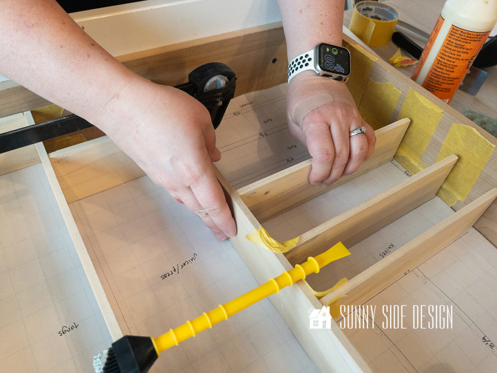 Woman places piece of wood with glue to adjoining piece forming a section for the DIY drawer dividers.