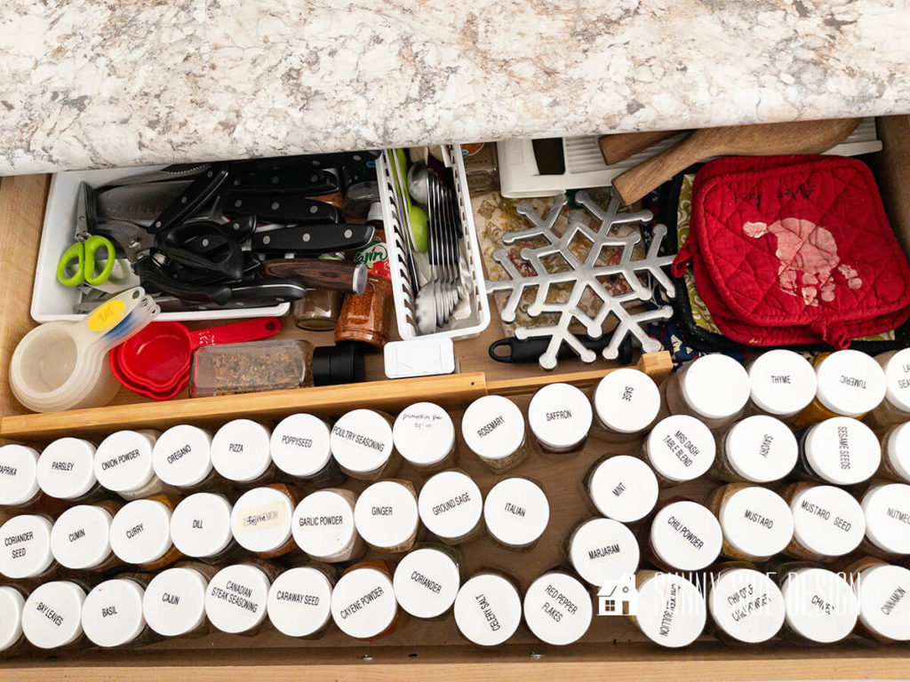 Kitchen drawer before building custom drawer dividers. Spices slide around, knives are all piled into a small plastic bin, measuring cups, hot pads and trivets.