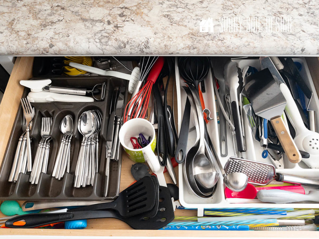 Kitchen utensil drawer with store bought organizers that are inefficient and waste space. Eating utensils, whisks, can opener, slicer, potato masher, ladels, grater, scoops, straws, spatulas and tongs