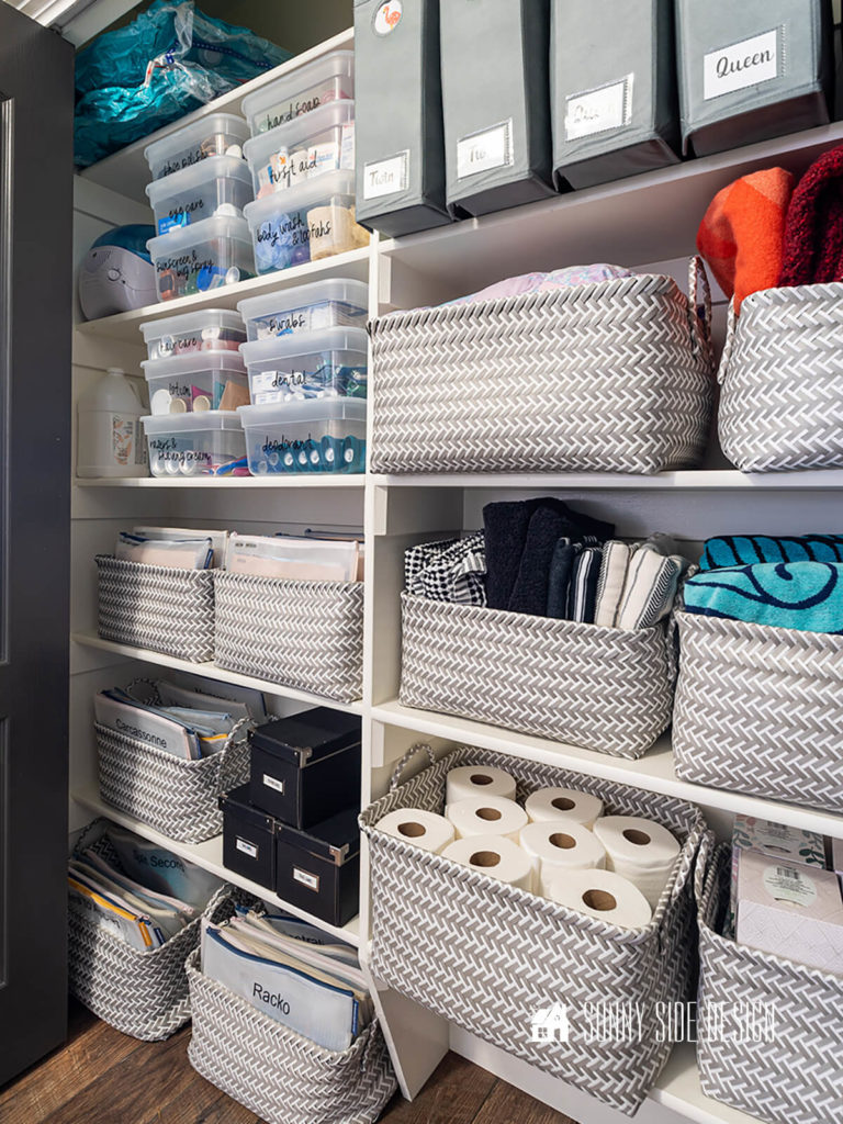 Neat and tidy organize linen closet with baskets and labeled clear lidded containers.