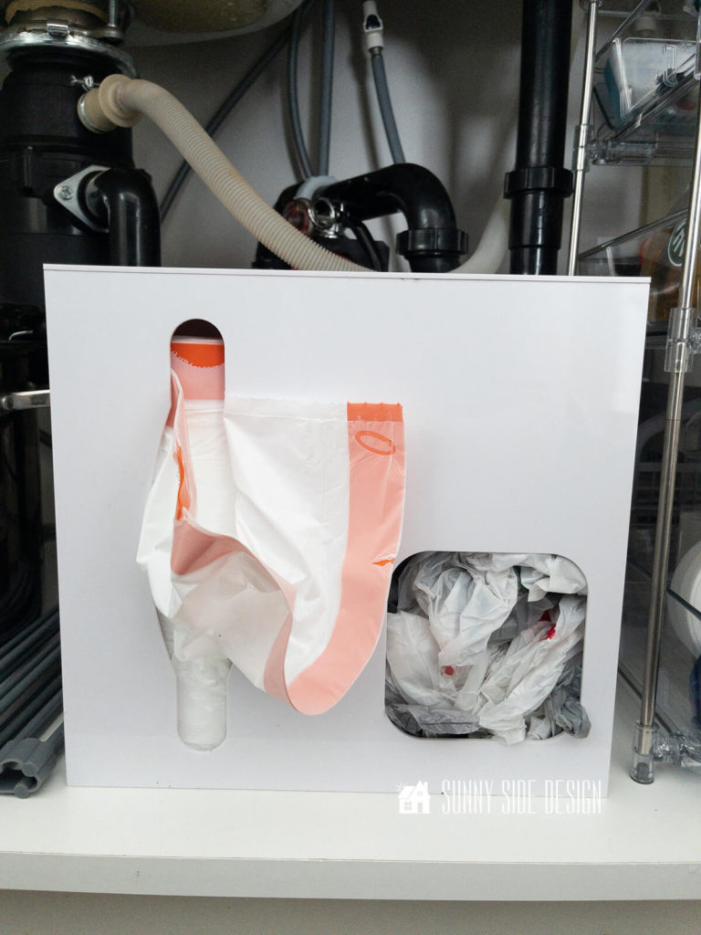 White plastic contain for storing trash and grocery bags under the kitchen sink.
