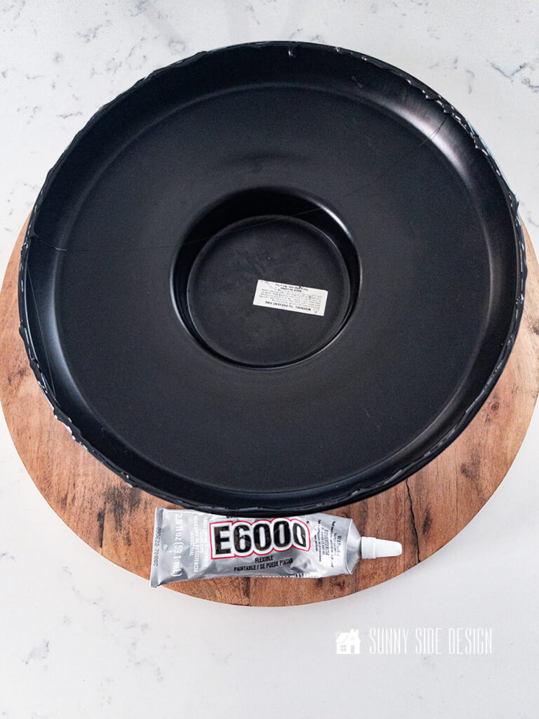 E6000 glue is applied to the rim of the black metal stand to adhere the round wooden piece.