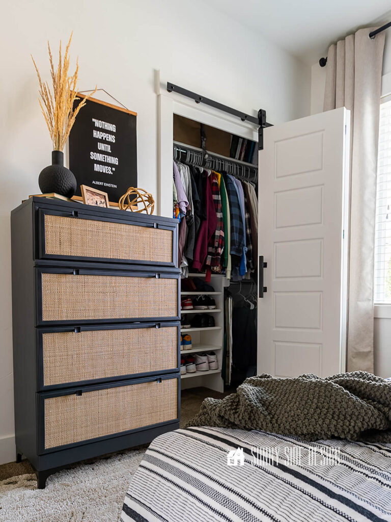 Custom DIY closet organizer in a small boys bedroom closet with bifold barn doors to make access easier. Modern black and rattan dresser against white wall.
