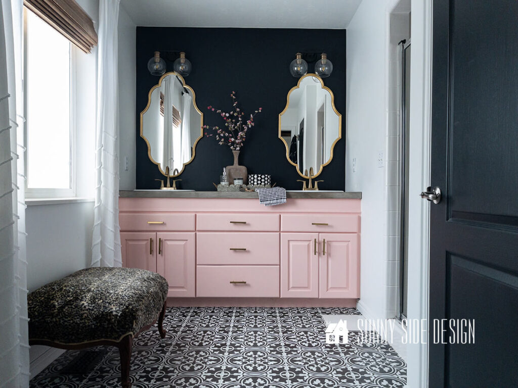 Cosmetic updates to Master bathroom, with black and white vinyl decals on floor, white paint, black door, pink painted vanity, gold hardware, mirrors and lights, faux fur ottoman, black accent wall above vanity.