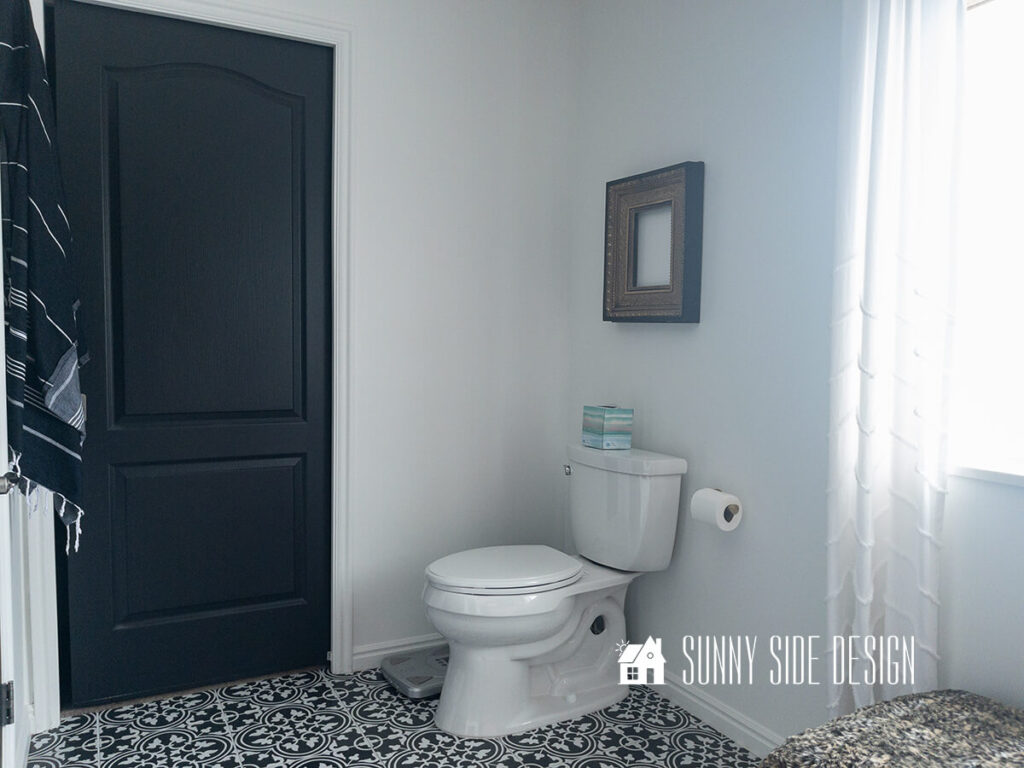 Master bathroom after cosmetic updates with black and white vinyl decals on floor, white paint, black door, gilded black frame above toilet.